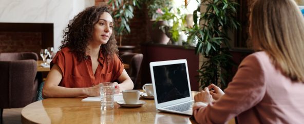 Women Sitting on Table with Cups of Coffee and Laptop